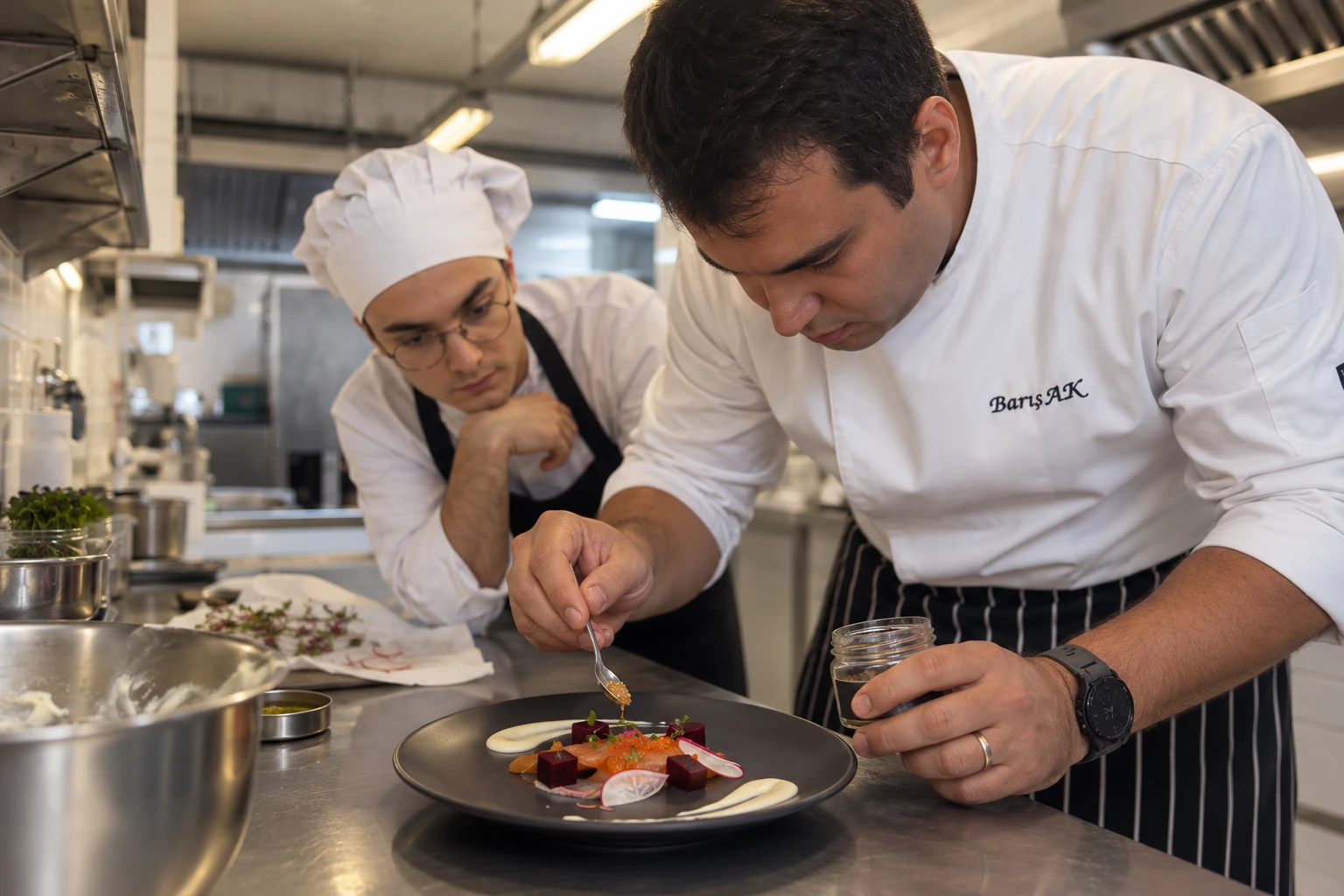 Barış Ak plating a dish while a culinary student closely observes