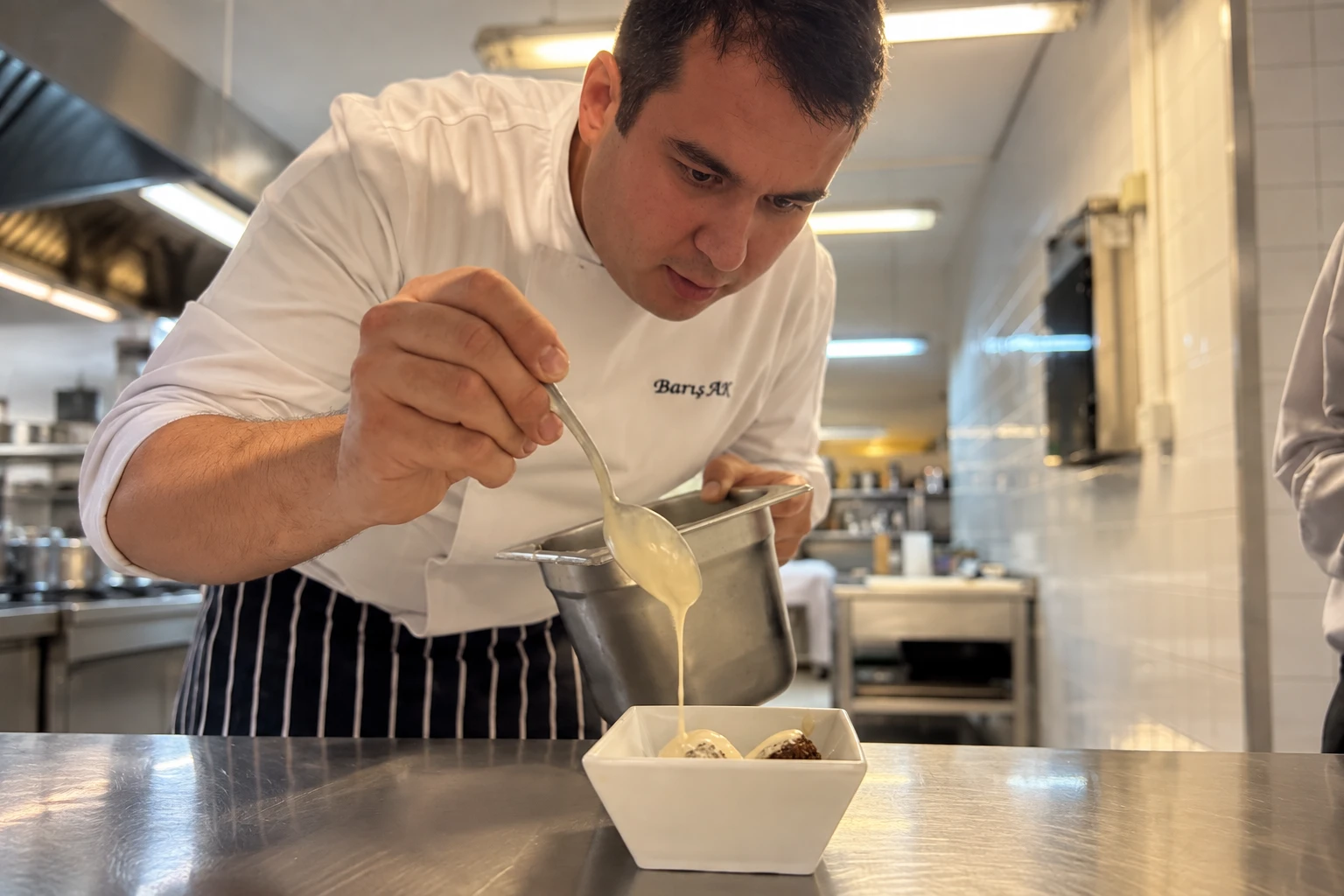 Barış Ak finishing a dessert with sauce in a professional teaching kitchen